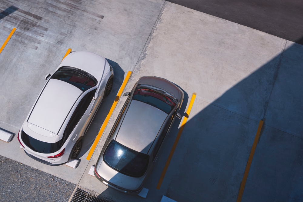 Aerial View of 2 Cars Parked on Concrete Floor in Outdoors Parking Lot area with Empty Space, Directly Above view of Car park Background with Sunlight and Shadow on Surface
