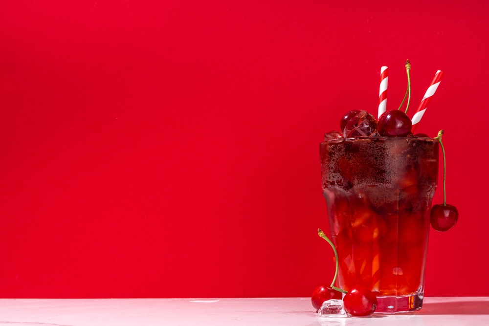 Iced cherry cola drink, Cold summer fruity non-alcohol cocktail with fresh cherries, juice, cola and ice, on high-colored background copy space
