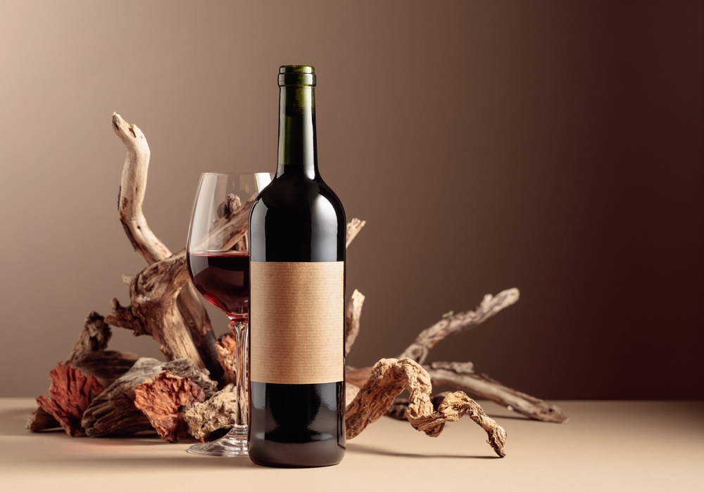 Bottle and glass of red wine with a composition of old wood. Minimalistic composition on a beige background for product branding, identity, and packaging. Copy space.

