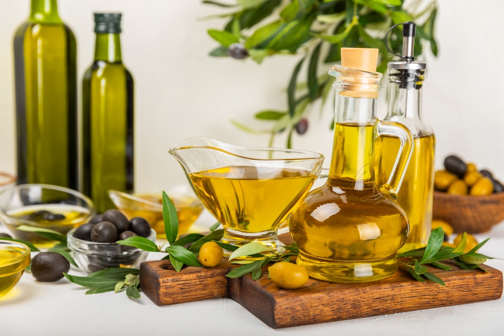 Olive oil in a bottle and gravy boat on the kitchen table. Oil bottle with branches and fruits of olives. Place for text. copy space. vegetable oil and salad dressing.