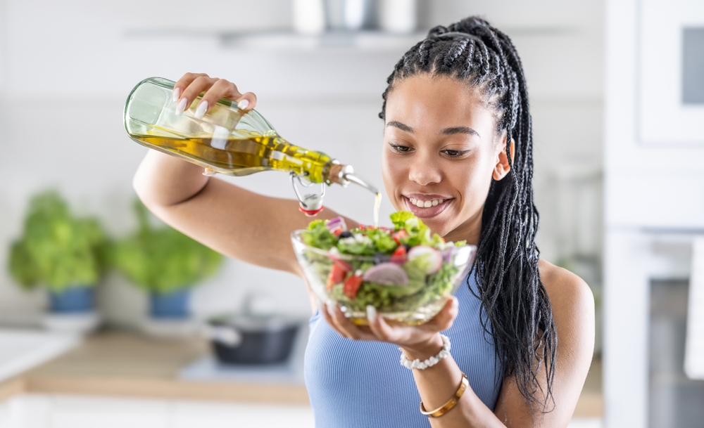 A young African American woman prepares a healthy leafy salad, tossing it with olive oil.
