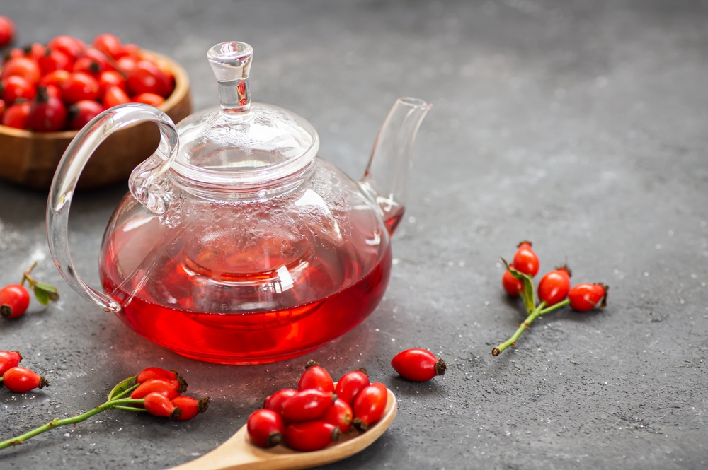 Rosehip tea in a teapot, herbal tea medicinal plants with rosehip fruits on rustic table. Dogrose winter tea background
