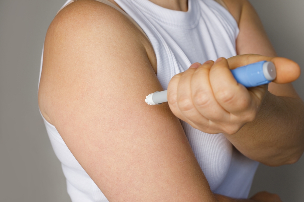 Female model making self injection with blue injection pen closeup. Medicine and treatment concept
