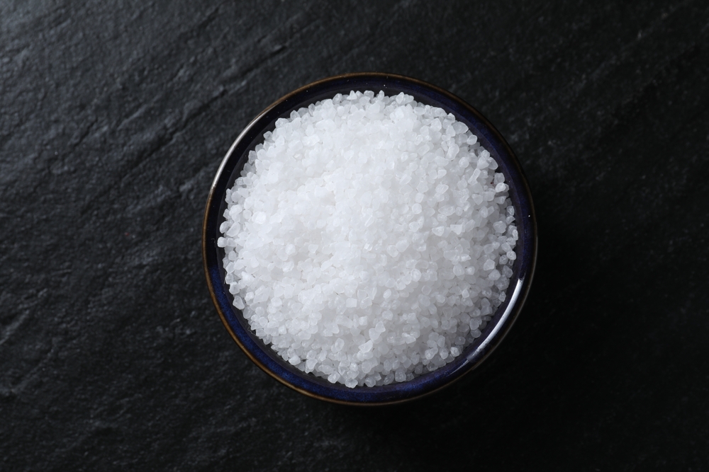 Organic white salt in bowl on black table, top view