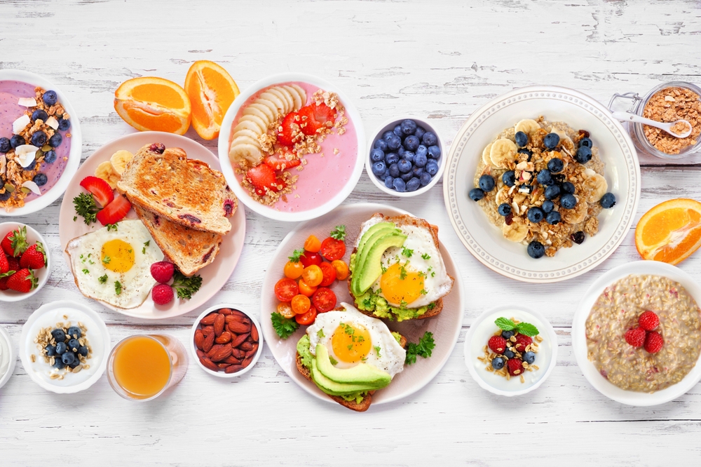 Healthy breakfast or brunch table scene on a white wood background. Top down view. Avocado toast, smoothie bowls, oats, yogurt and a variety of nutritious foods.
