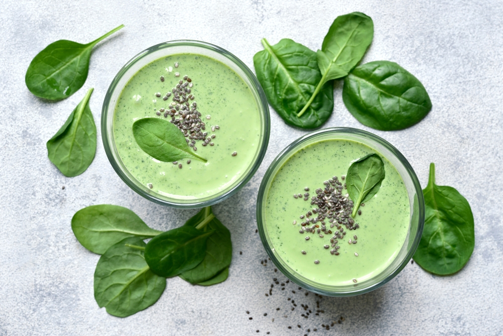 Detox spinach smoothie in a tall glass on white slate, stone or concrete background. Top view with copy space.
