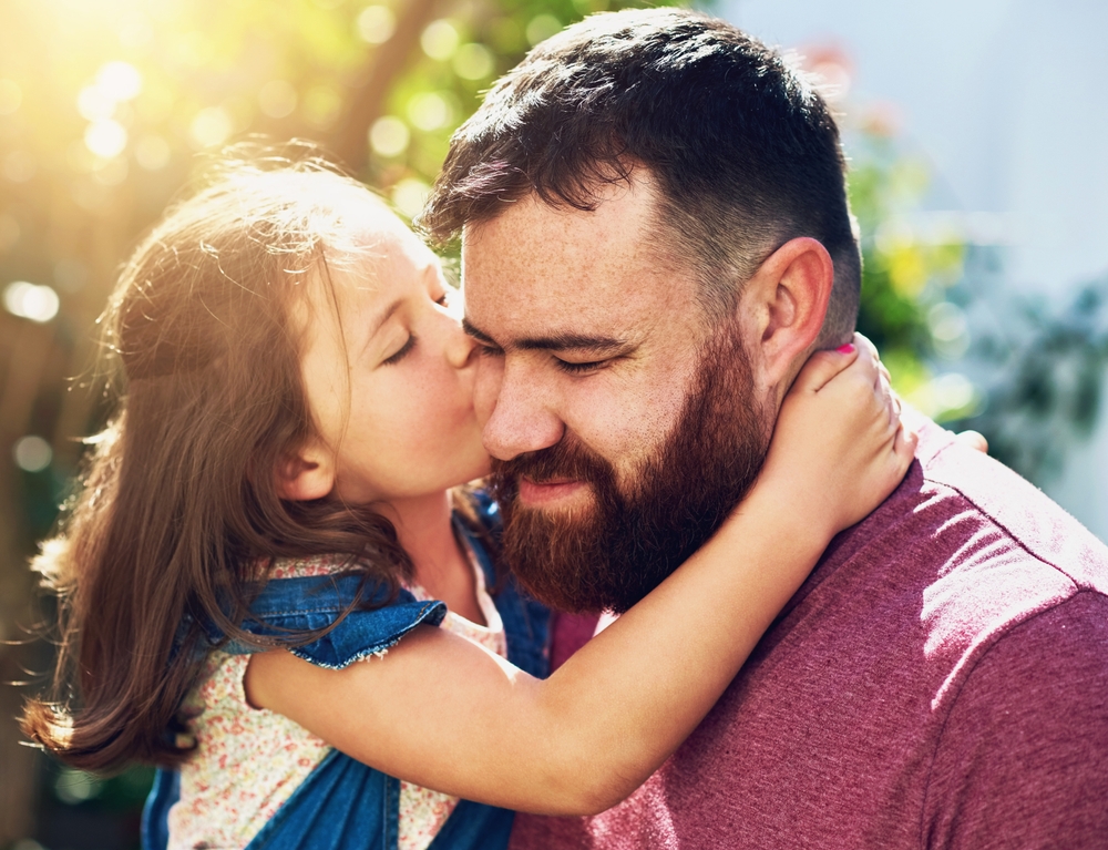 Father, daughter and kiss with affection, care and love in garden or backyard for bonding as family. Male parent, girl and hug in embrace for together, memory and support for childhood development