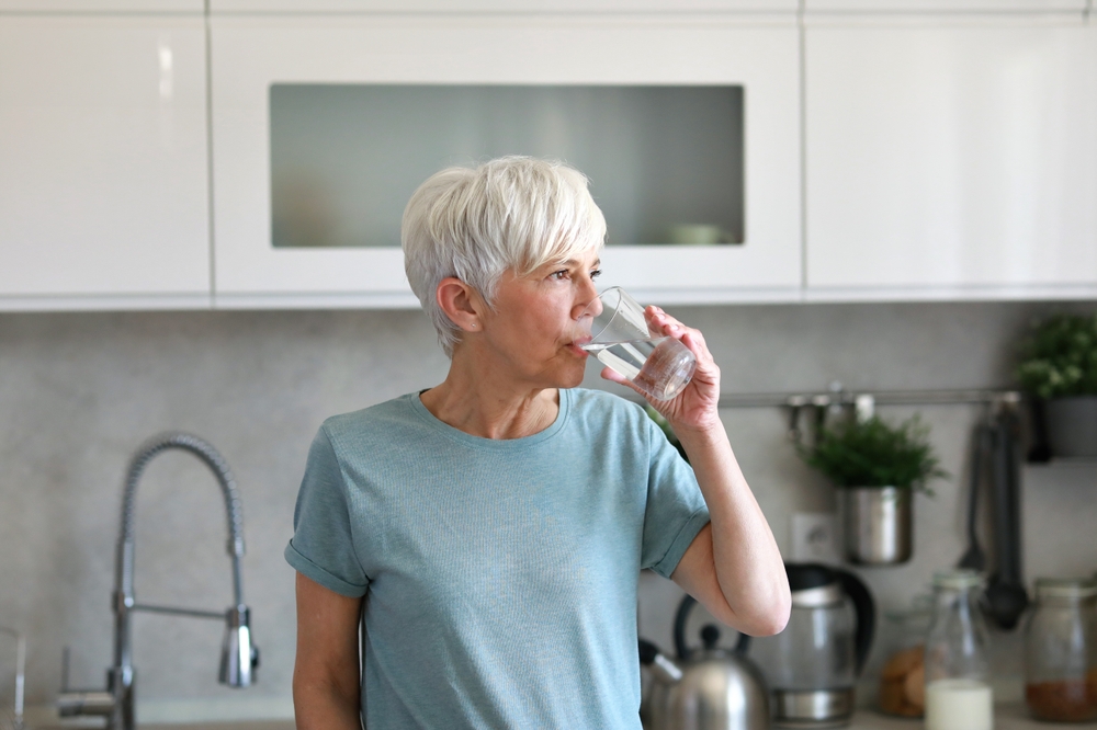 Portrait of a happy senior mature mid aged woman holding a glass and drinking water and having a healthy breakfast after fitness exercise training in the morning at home