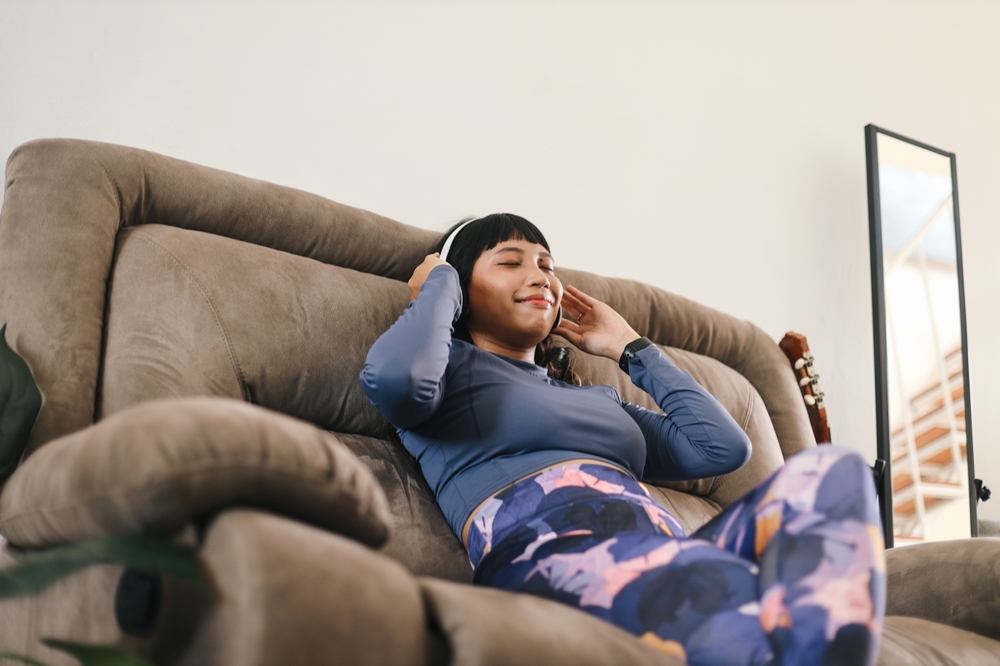 Young Woman Wearing Headphones And Sitting On Couch Resting After A Workout At Home
