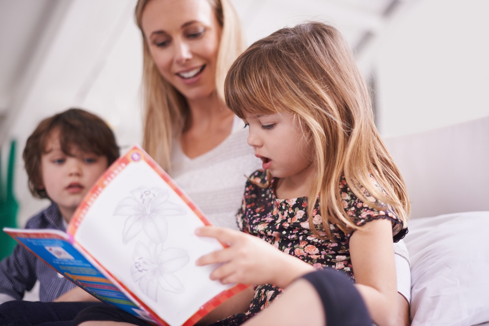 Reading, woman and children on sofa with book for bonding, teaching and learning together in home. Mother, son and daughter relax on couch with storytelling, smile and happy family in living room