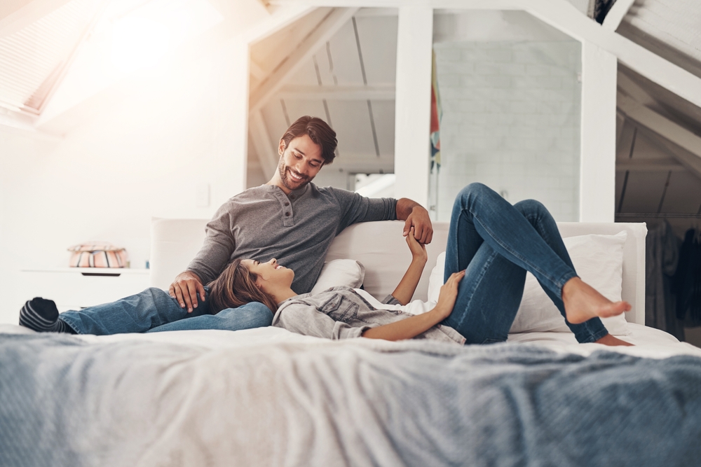 Relax, couple and holding hands in bed in the morning with love, bonding and care together in a home with a smile. Chat, marriage and romance of happy people in a bedroom with support and commitment