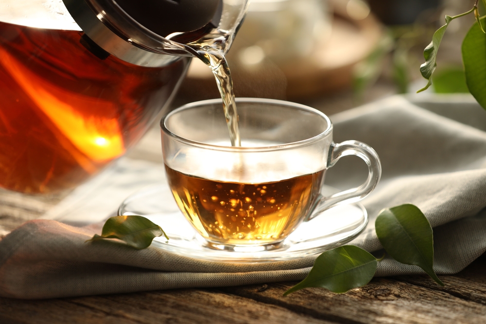 Pouring tea into cup on wooden table, closeup

