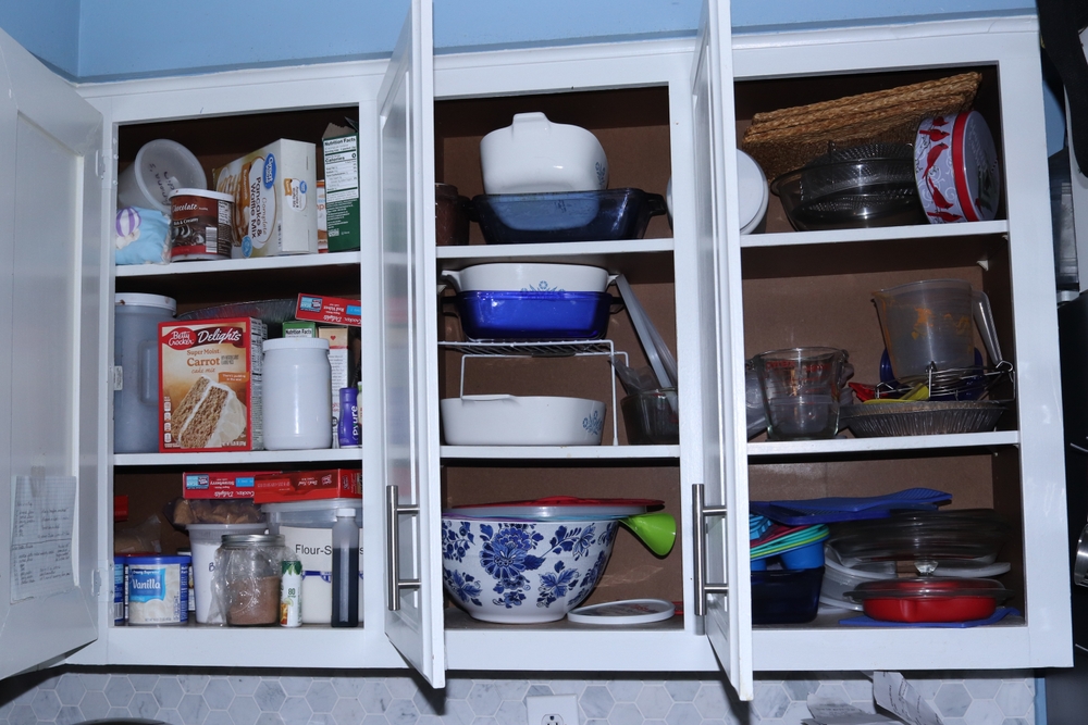 Dalton, OH USA - 07 15 2024: 3 Open white cabinets of Cluttered items Overfull in a real Kitchen
