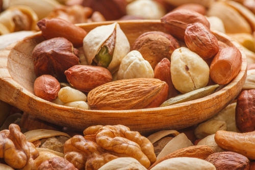 Nuts and seeds of different types with a wooden spoon closeup with selective focus - peeled walnut, hazelnuts, peeled peanut, pine nut kernels, almond seeds, cashew seeds, pistachio nuts in the shell
