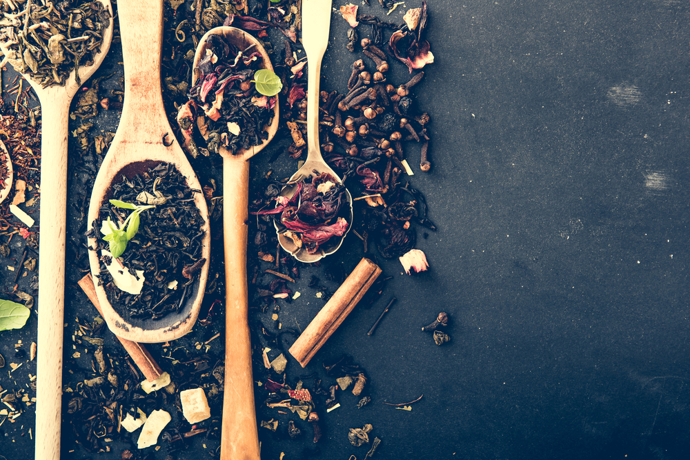 Virious kinds of tea in wooden spoons on black table
