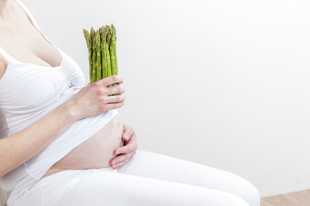 close up of pregnant woman holding green asparagus