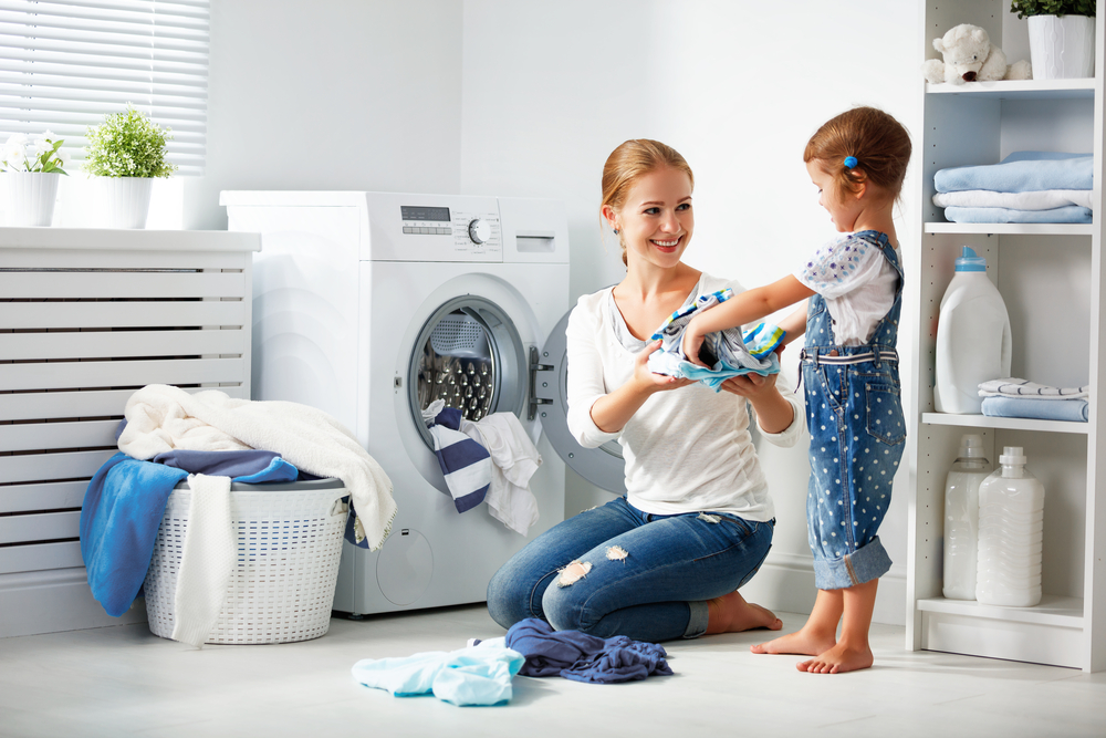 family mother and child girl little helper in laundry room near washing machine and dirty clothes