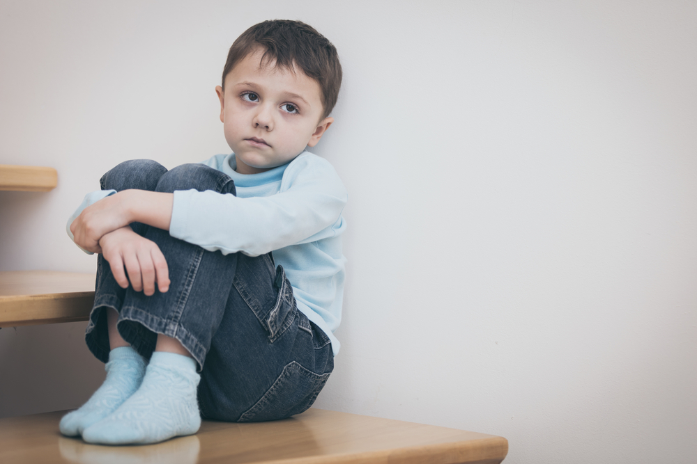 one sad little boy sitting on the stairs in house at the day time. Concept of sorrow.