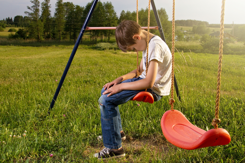Sad lonely boy sitting on swing alone
