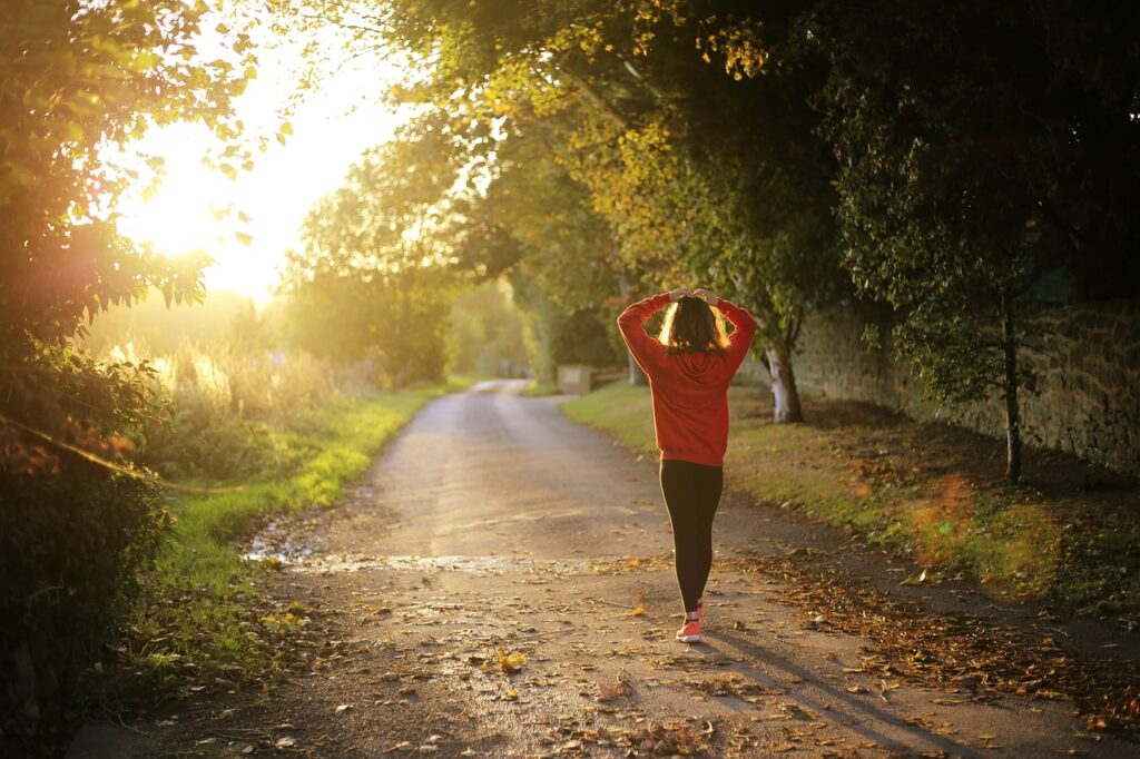 Woman walking on a path in the sun. Greenery in the background.