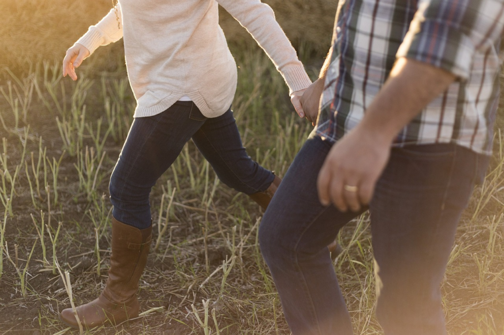 two people holding hands walking in a field