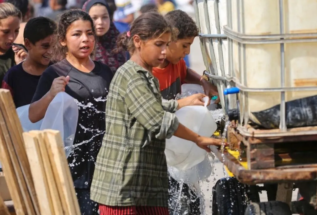 People line up to fill containers with water at a makeshift camp for displaced Palestinians in Deir al-Balah in the central Gaza Strip