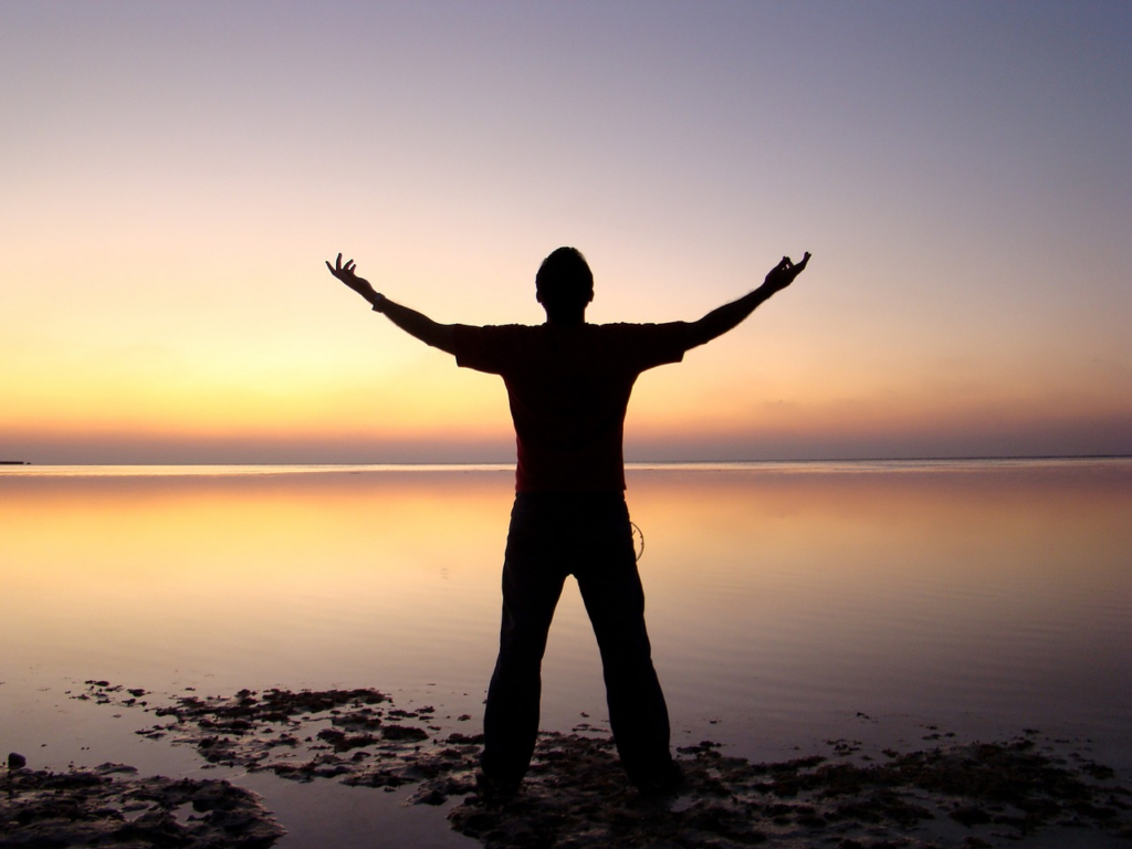 silhouette of one person standing in front of the water at sunset