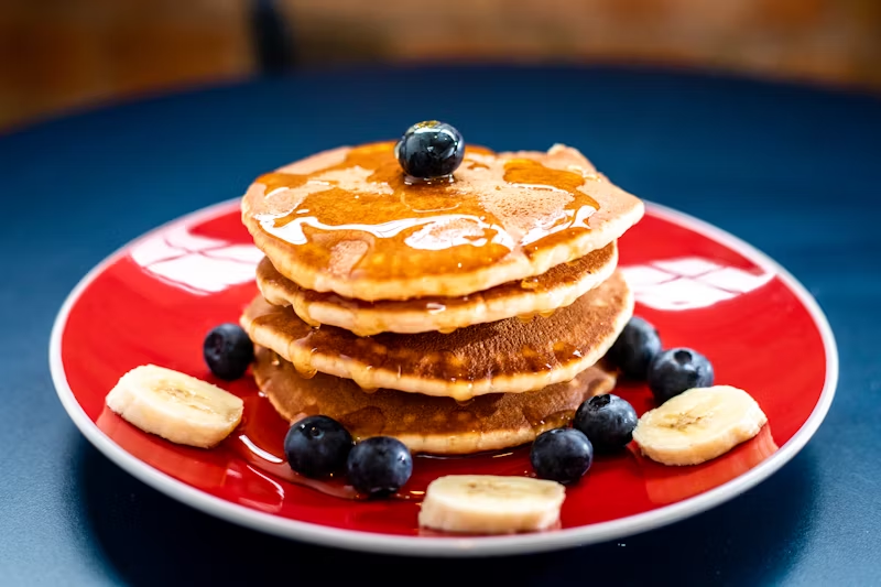 pancakes with banana slices, blueberries, and maple syrup on top