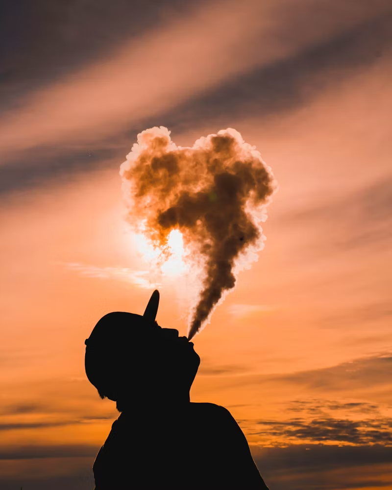 man blowing smoke into the sunset air