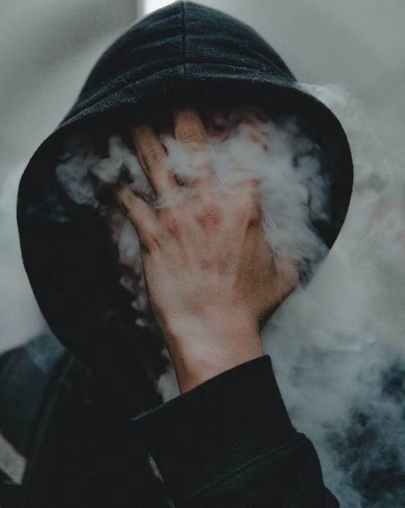 a person with a hand in their smoke-covered face