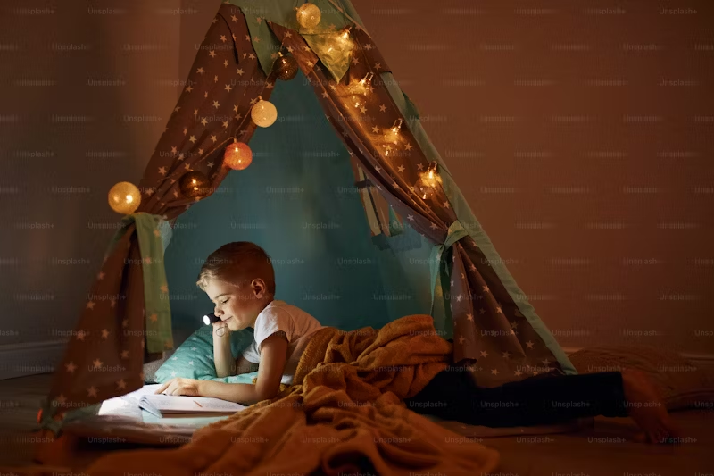 boy using flashlight to read text book