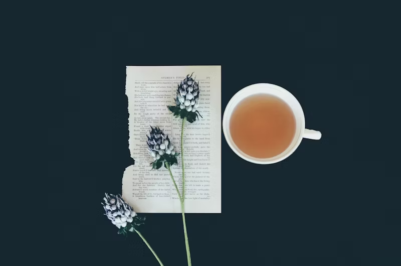 a cup of tea with flowers with a ripped page under it