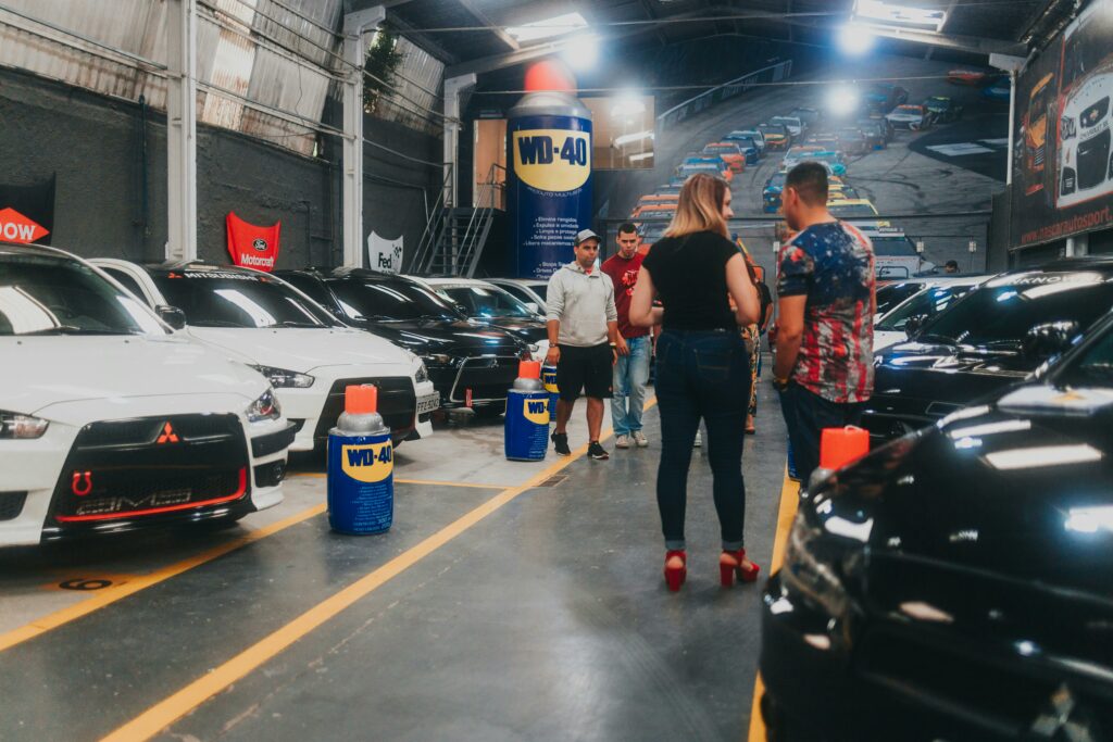 People conversing in automotive showroom featuring various Mitsubishis. Advertisements for WD-40 seen