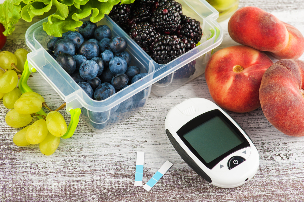 Blood glucose meter and berries in lunch box and fruits and vegetables on wooden table