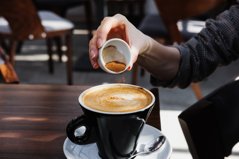 Woman adds cinnamon to cappuccino. A cup of cappuccino coffee on the table.