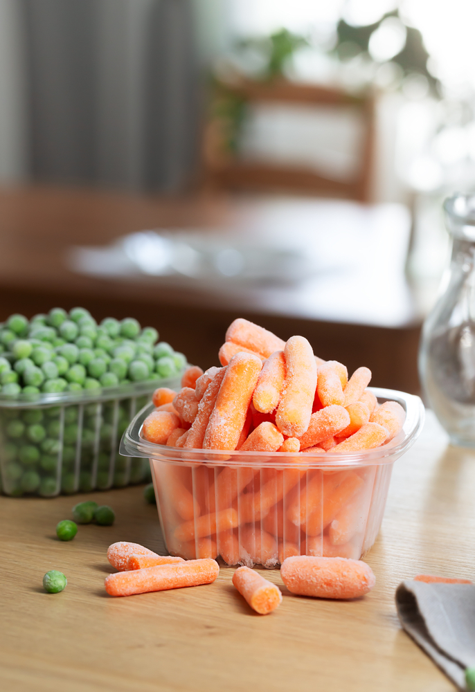 Frozen vegetables such as baby carrot and peas in the storage boxes on the kitchen table. Freezing is a safe method to increase the shelf life of nutritious foods
