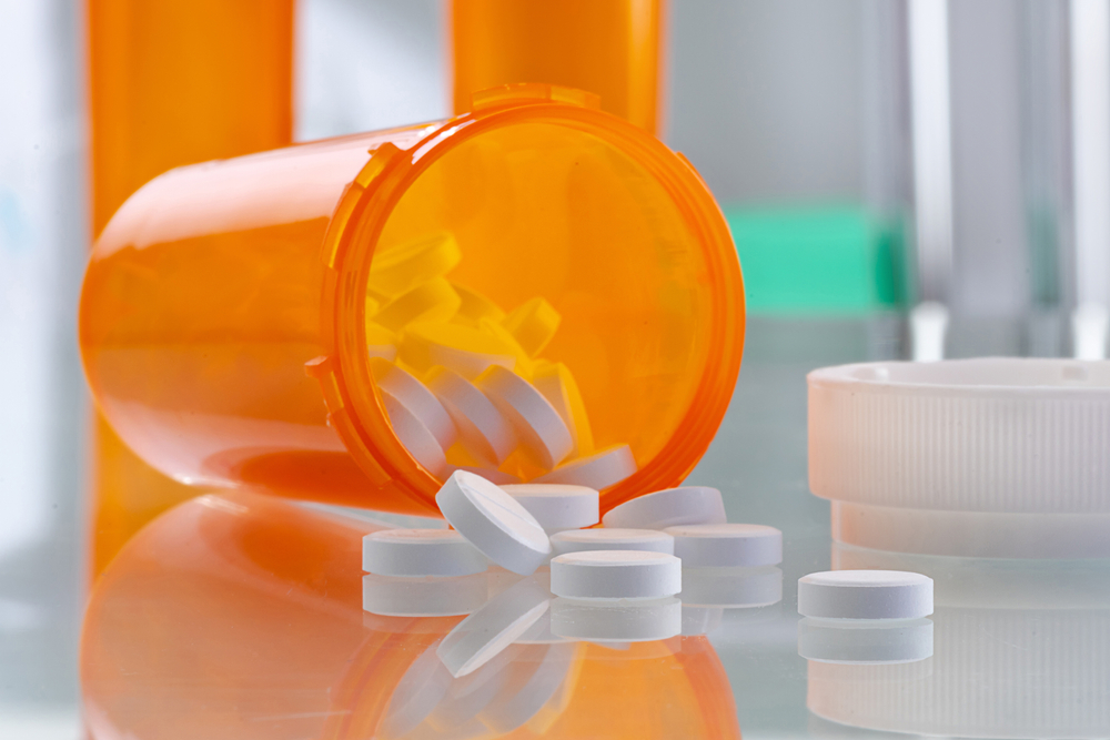 Healthcare and medical concept - orange prescription bottle with pills and drugs in the hospital. Glass tabletop with reflections in sterile room. Close up view