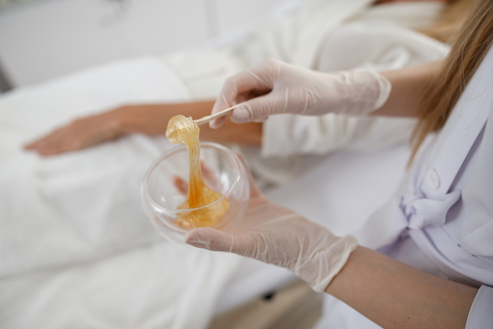 Sugaring with natural materials. Doctor puts wax, honey. Concept of medicine, medical instruments, health care, beauty industry, hair removal
