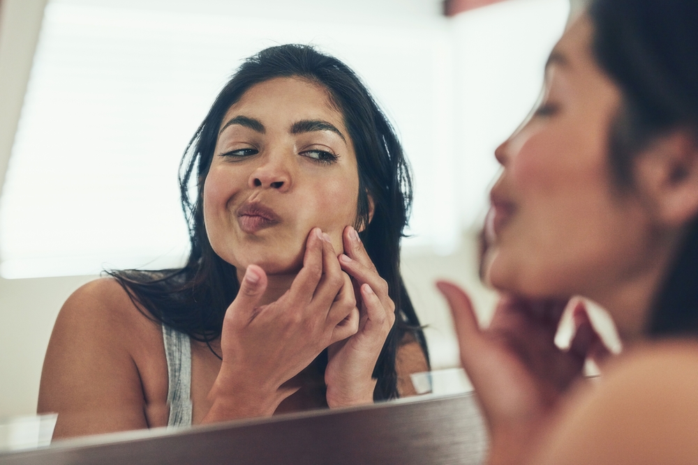 Where did this pimple pop up from. Shot of a young woman squeezing a pimple on her face at home.