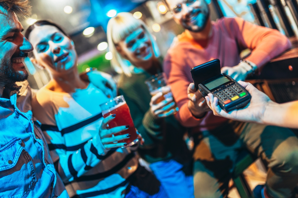 Diverse friends in bar paying with cellular device