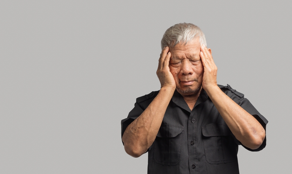 Stroke, brain attack, migraines brain diseases problem cause chronic severe headaches. Portrait of an elderly Asian man suffering headache pain while standing against a gray background
