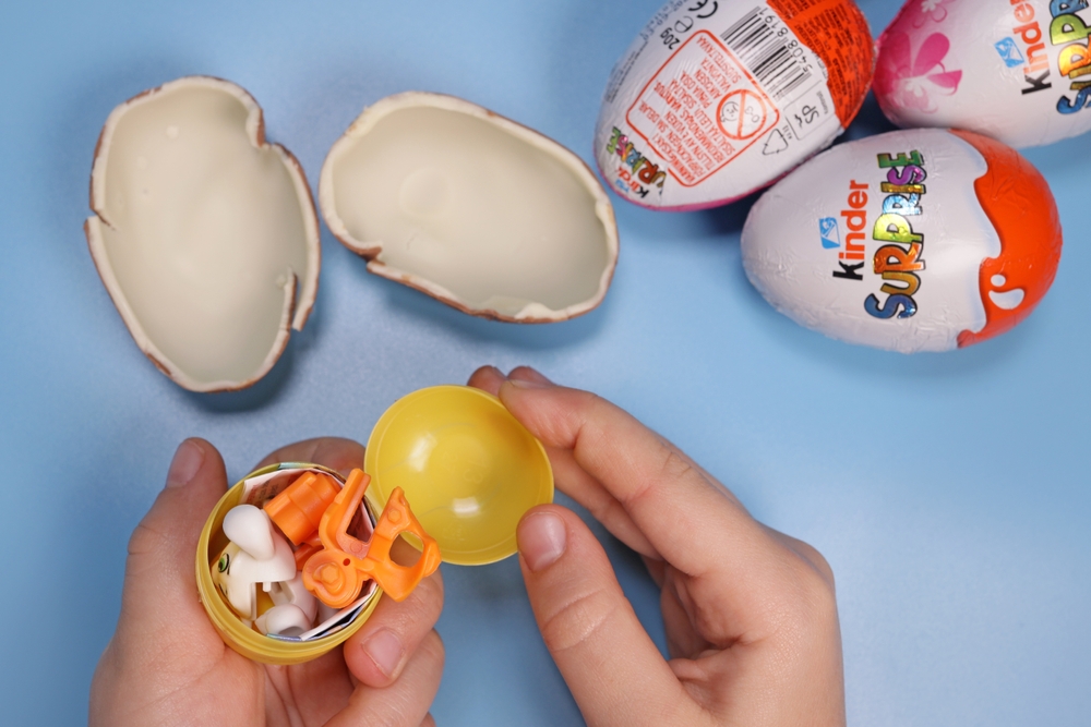 Magdalinovka, Ukraine - March 3, 2023. child holds a Kinder Surprise capsule with a toy on a blue background