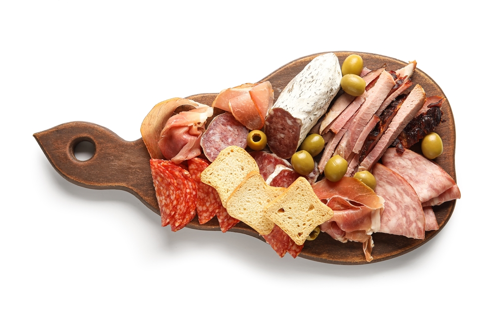 Wooden board with assortment of tasty deli meats isolated on white background