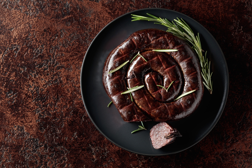 Black pudding or blood sausage with rosemary on a black plate. Top view. Copy space.