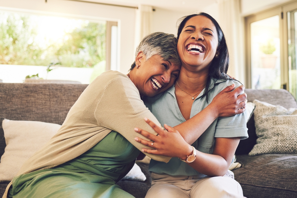 Senior mother, funny and hug woman in living room, bonding and laughing together. Happy, elderly mom and embrace person, relax and smile with care, love and enjoying time on home sofa with family.