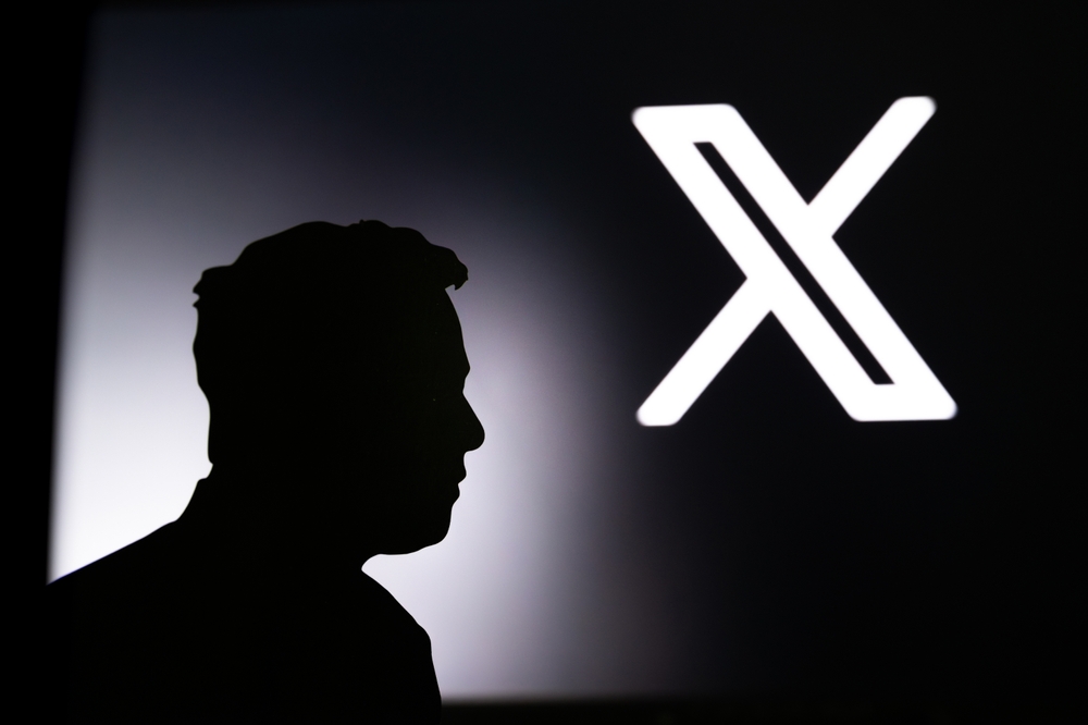 CALIFORNIA, USA, 24. JULY 2023: New logo of Twitter. Silhouette of Elon Musk in front of black banner with Twitter new X logo in background.
