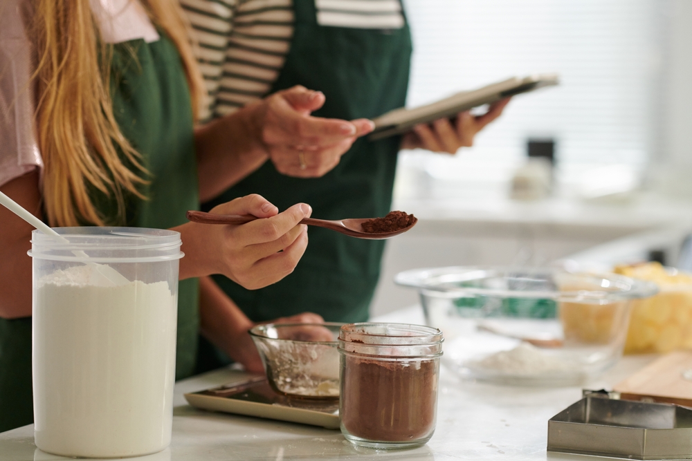 Teenage girl putting teaspoon of cinnamon in bowl with cookie dough