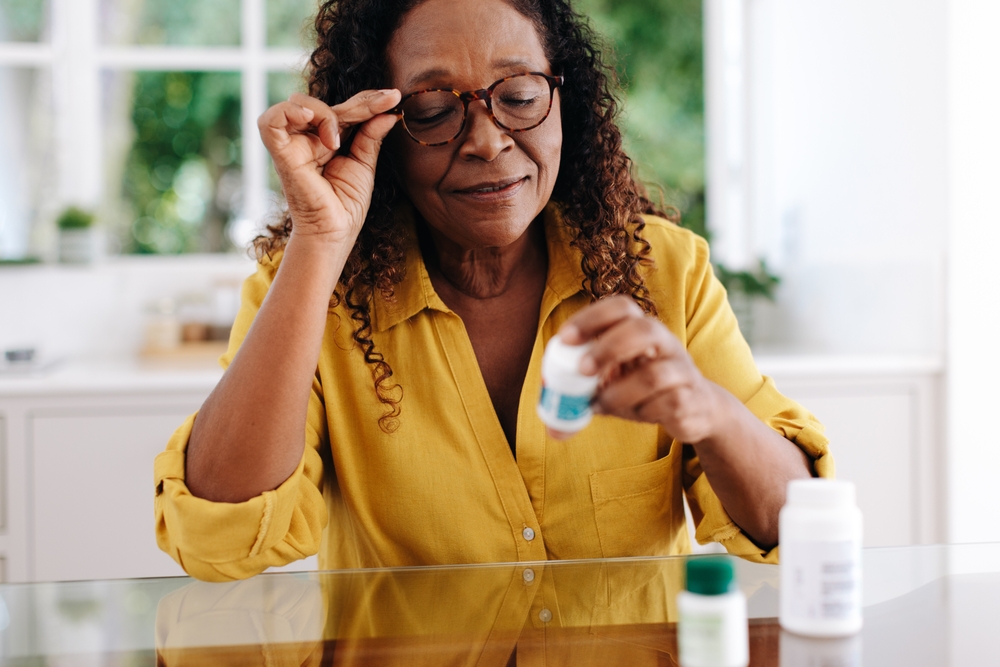 Woman reading the label on her prescription medication as she adheres to her treatment routine at home. Senior woman taking proactive steps to manage her chronic disease and maintain her health.
