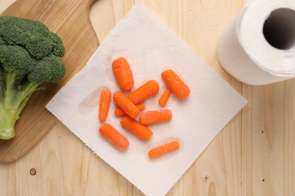 Carrots drying on paper towel and broccoli on wooden table, flat lay