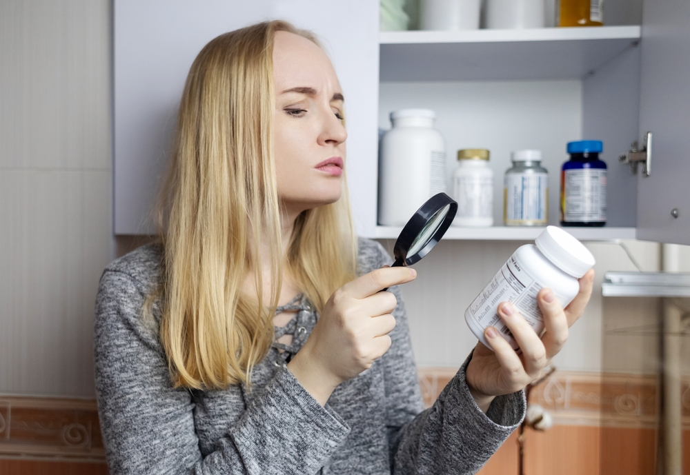 Girl studies dietary supplements. Reading the instructions on a bottle of vitamin complex. Nutritional supplement for hair loss and weakened immunity. Self-prescription of drugs and harm to health